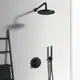 Schwarze Duscharmatur von Ideal Standard mit Regendusche, Handbrause und Bedienknöpfen an einer hellen Wand, daneben ein Handtuchhalter aus schwarzem Metall.